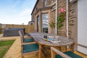 Eine Terrasse im Freien mit Holztisch, grünen Sitzgelegenheiten mit Polstern und einem Grill.