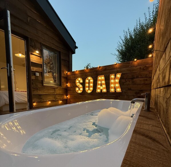 A wooden cabin with a large illuminated sign reading 'SOAK' and a hot tub filled with water and ice.