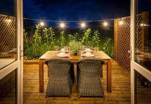An outdoor dining area with a wooden table and wicker chairs, surrounded by a wooden deck and a view of a garden. - 2 Bed in Wichenford (oc-t45441) (Ockeridge)