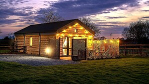 A log cabin with a porch, a fenced area with bicycles, and a gravel driveway. - 2 Bed in Wichenford (oc-t45441) (Ockeridge)