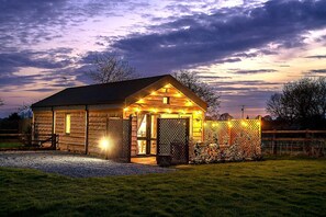 A log cabin with a porch, a fenced area with bicycles, and a gravel driveway. - 2 Bed in Wichenford (oc-t45441) (Ockeridge)