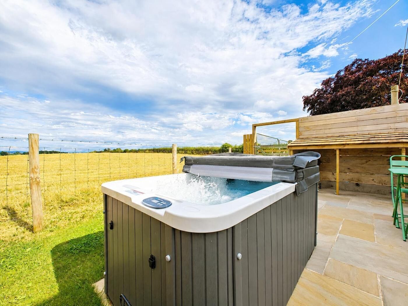 Un bain à remous doté d’un panneau de commande, entouré d’une terrasse en bois et d’un champ d’herbe.