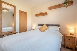 A bedroom with a large bed, bedside tables, a mirror, and a wooden shelf with a plant. - 1 Bed in Thursby (oc-b45540) (Bank End)