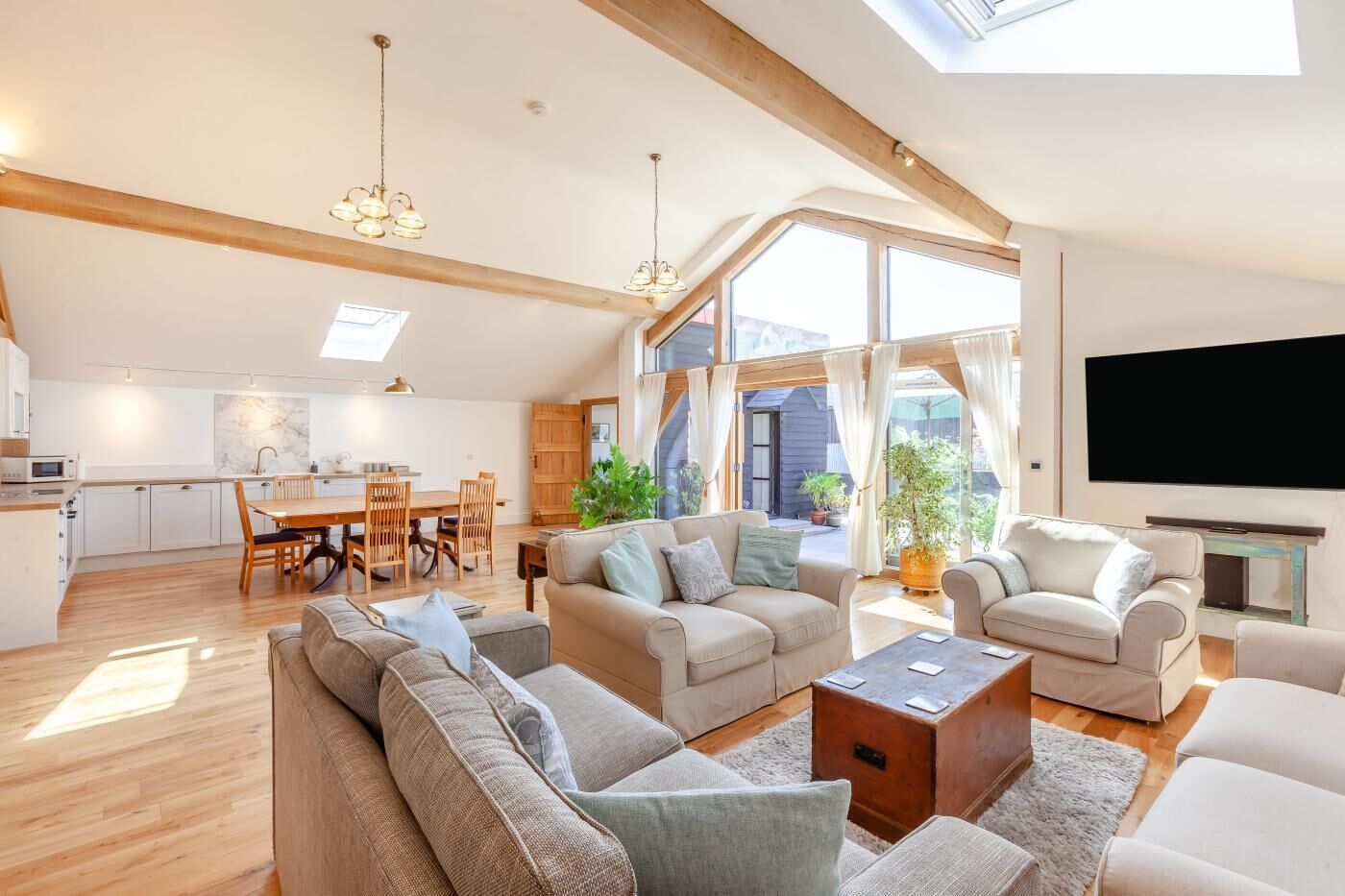 A spacious living area with a high ceiling, wooden beams, a dining area, and a large window providing natural light.