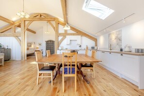 Ein großzügiger Loft-Raum mit Esstisch aus Holz, Stühlen und einer Küchenzeile mit weißen Schränken.