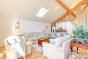 A spacious living room with a high ceiling, wooden beams, a skylight, and a cozy arrangement of sofas and a coffee table. - 1 Bed in Langford (oc-p45260) (Langford)