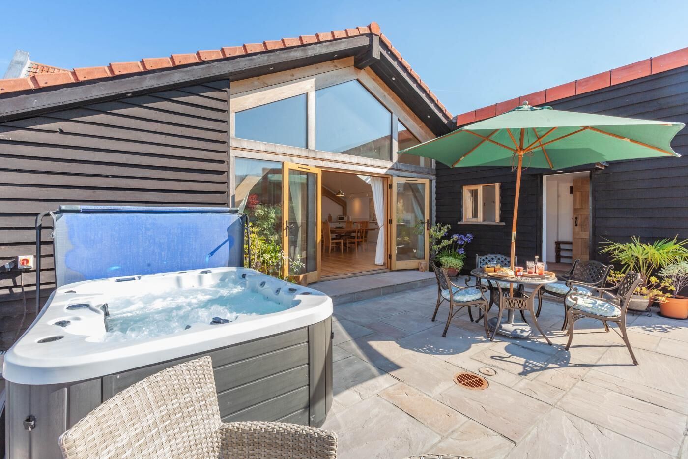 Eine Terrasse mit Whirlpool, Sitzgelegenheit im Freien und einer Glastür zu einem Innenbereich.