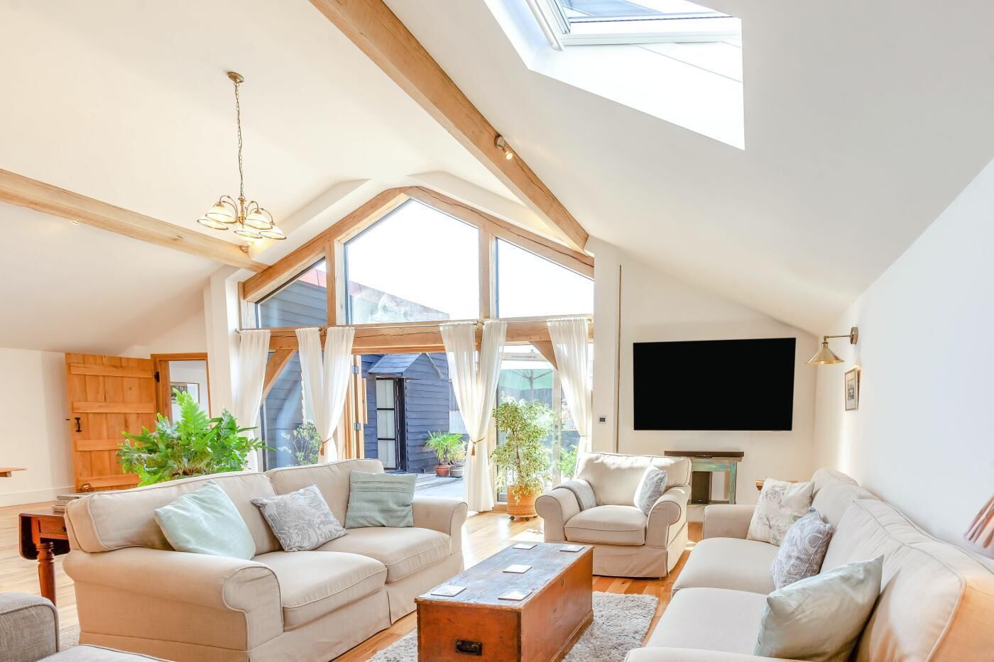 Ein geräumiges Wohnzimmer mit hohen Decken, großen Fenstern und einem an der Wand befestigten Flachbildfernseher.