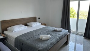 Quarto de hotel com cama, mesa de cabeceira, ar-condicionado fixado na parede e vista pela janela com cortinas.