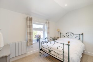 Une chambre à coucher avec un lit en métal, un radiateur, une fenêtre avec des rideaux et une table de chevet avec une lampe.