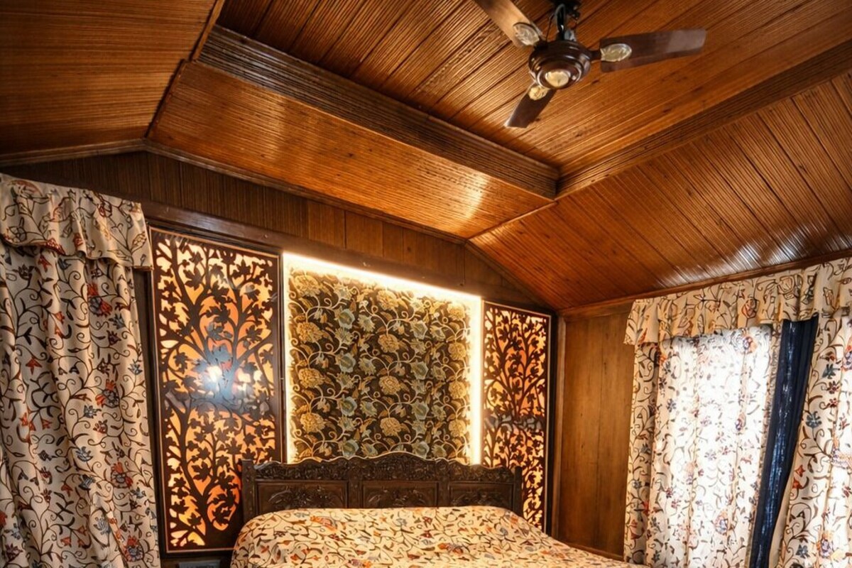 Um quarto com teto de madeira, uma cama com colcha estampada e um tapete vermelho com padrão.