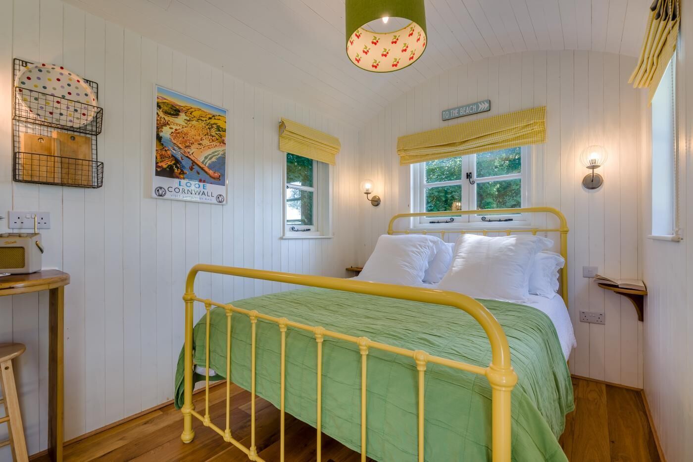 A room with a bed, a table, a lamp, a poster, and a window with a view.