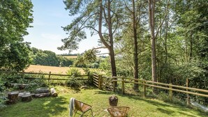 A grassy outdoor area with a wooden fence, two wicker chairs, and a rustic wooden bench. - 1 Bed in Trewidland (oc-r45330) (Saint Keyne)