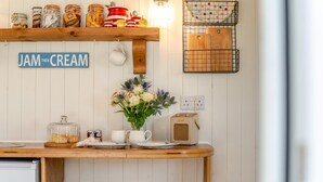 A kitchen with a wooden countertop, a sign reading 'JAM THEN CREAM', jars of preserves, a radio, and a vase of flowers. - 1 Bed in Trewidland (oc-r45330) (Saint Keyne)