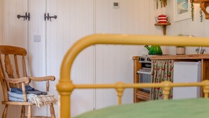 A wooden bed frame with a green bedspread, a wooden chair with a blanket and shoes, a small table with a green vase, and a white refrigerator. - 1 Bed in Trewidland (oc-r45330) (Saint Keyne)