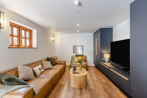 A modern living room with a sofa, coffee table, and a flat-screen TV. - 5 Bed in Bishops Lydeard (oc-b45427) (Triscombe)