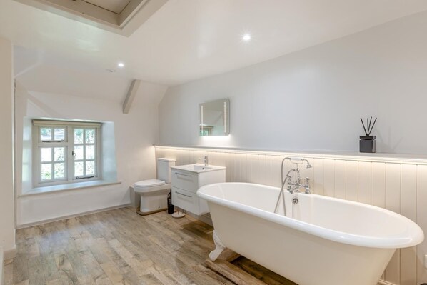 Et moderne badeværelse med badekar, toilet, håndvask og et vindue.