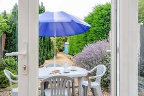 A patio with a table and chairs, a blue umbrella, and a garden view. - 2 Bed in Snettisham (oc-d45324) (Snettisham)