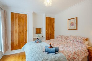 A bedroom with a bed, a wooden wardrobe, a mirror, and a framed picture on the wall. - 2 Bed in Snettisham (oc-d45324) (Snettisham)