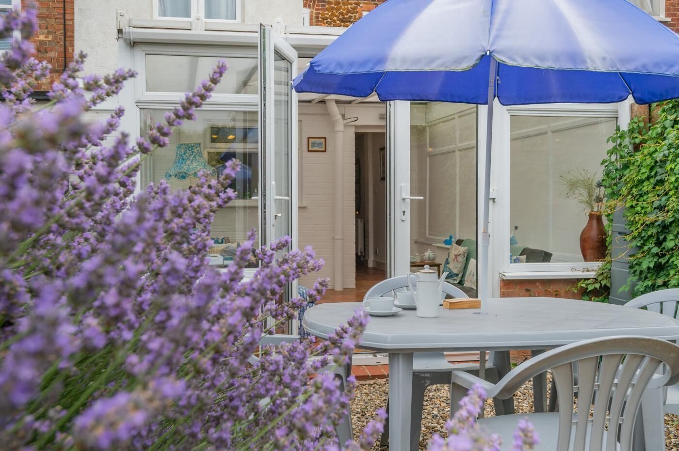 Un espace extérieur aménagé avec une table et des chaises, un parasol bleu et une vue sur une maison dotée d’une porte en verre.