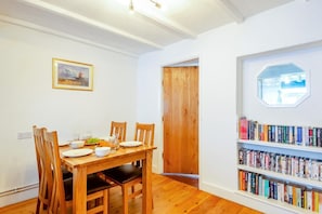 Ein Essbereich mit Holztisch und -stühlen, einem Bücherregal mit Büchern, einem gerahmten Bild an der Wand und einer Holztür.