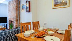 A dining area with a brick fireplace, wooden chairs, a table set for a meal, and a painting on the wall. - 2 Bed in Snettisham (oc-d45324) (Snettisham)