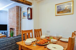 A dining area with a brick fireplace, wooden chairs, a table set for a meal, and a painting on the wall. - 2 Bed in Snettisham (oc-d45324) (Snettisham)