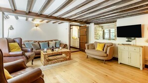 A living room with a wooden coffee table, leather sofas, a television, and a stone wall. - 3 Bed in Combe St. Nicholas (oc-s45333) (Combe Saint Nicholas)