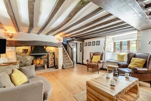 Ein gemütliches Wohnzimmer mit Kamin, Holzbalken, einer Treppe und bequemen Sitzgelegenheiten.