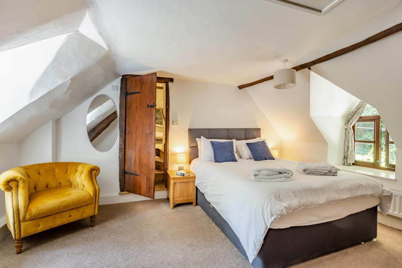 A bedroom with a bed, a chair, a nightstand, and a window.
