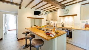 A kitchen with a wooden island, bar stools, a clock, and a microwave. - 3 Bed in Combe St. Nicholas (oc-s45333) (Combe Saint Nicholas)