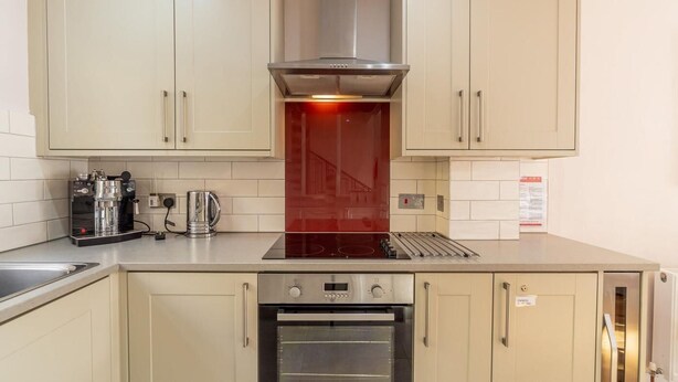 A kitchen with beige cabinets, a stainless steel range hood, a built-in oven, and a coffee machine. - 2 Bed in Ambleside (oc-lr114) (Chapel Stile)