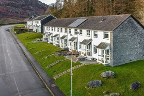 Reihenweise weiße Gebäude mit Steinverkleidungen, eine gepflasterte Straße und eine Rasenfläche mit Steinen.