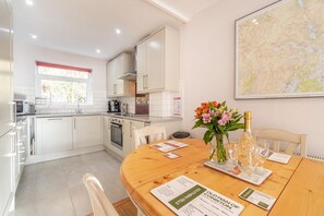 A modern kitchen with white cabinets, a dining table with placemats, a vase with flowers, and a map on the wall. - 2 Bed in Ambleside (oc-lr114) (Chapel Stile)