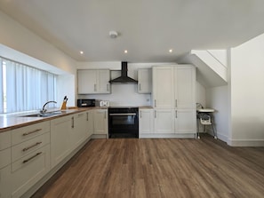 A modern kitchen with wooden flooring, white cabinetry, a black range hood, and a built-in oven. - 5 Bed in Llandderfel (oc-b45562) (Llandderfel)