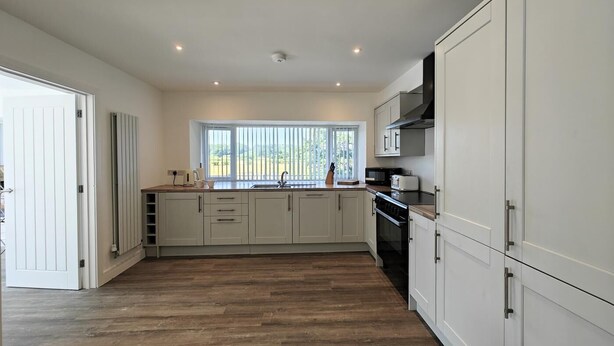 A modern kitchen with white cabinetry, a large window, and a view of greenery outside. - 5 Bed in Llandderfel (oc-b45562) (Llandderfel)