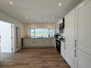 A modern kitchen with white cabinetry, a large window, and a view of greenery outside.