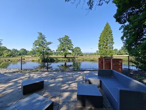 Eine Terrasse mit Gartenmöbeln, einer Backsteinmauer und Blick auf einen See.