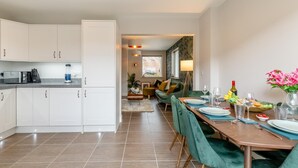 Una cocina moderna con armarios blancos y un comedor con una mesa de madera para cuatro comensales.