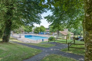 A swimming pool surrounded by a fence, with a grassy area and trees in the foreground. - 4 Bed in Newquay (oc-s45403) (Black Cross)