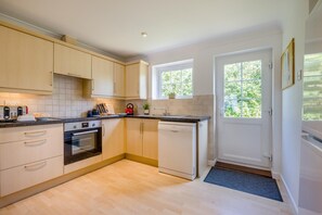 A modern kitchen with light wood cabinetry, a built-in oven, a dishwasher, and a window providing natural light. - 4 Bed in Newquay (oc-s45403) (Black Cross)