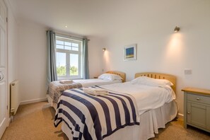 A bedroom with two beds, a window with curtains, a bedside table, and a wall-mounted light fixture. - 4 Bed in Newquay (oc-s45403) (Black Cross)