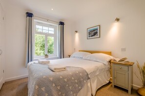 A neatly made bed with a patterned bedspread, a bedside table with a book, and a window with curtains. - 4 Bed in Newquay (oc-s45403) (Black Cross)