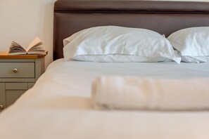A neatly made bed with white linens and pillows, a bedside table with a book, and a brown headboard. - 4 Bed in Newquay (oc-s45403) (Black Cross)