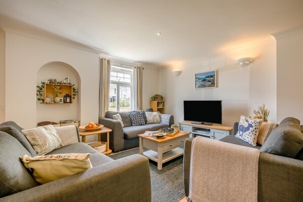 A living room with a sofa set, a coffee table, a flat-screen TV, and a bookshelf. - 4 Bed in Newquay (oc-s45403) (Black Cross)