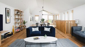 A spacious living area with a central coffee table, a dark blue sofa, and a wooden dining table with chairs. - 3 Bed in Mawgan Porth (oc-b599246) (Saint Eval)