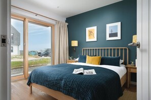 A bedroom with a large bed, two bedside lamps, and a view through a sliding glass door. - 3 Bed in Mawgan Porth (oc-b599246) (Saint Eval)