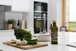 Eine Küchenarbeitsplatte mit frischem Gemüse, einer Olivenölflasche und einem weißen Keramiktopf.