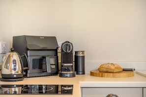 Eine Küchenzeile mit Kaffeemaschine, Wasserkocher, Toaster und einem Brotlaib auf einem Holzbrett.