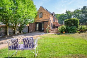 A brick house with a large garage door, a lawn, and a metal chair in the foreground. - 1 Bed in Bournheath (oc-h45428) (Catshill)